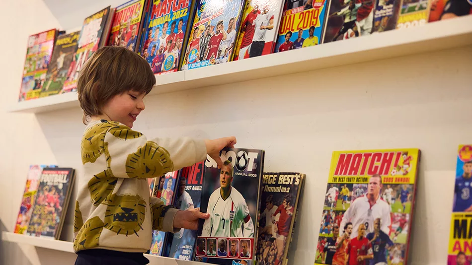 A boy choosing a football annual to read from the shelf